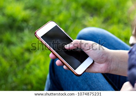 Mobile phone in woman's hand in a deckchair against the background of green grass. Time to rest. Work on vacation,  resting woman, lying feet girls, outdoors, park, using a smart phone,  summer
