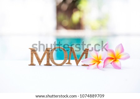 Beautiful Plumeria flower with wooden text over blurred swimming pool background, mother's day concept