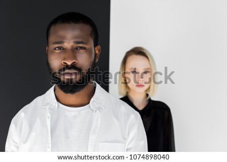 multicultural couple looking at camera near black and white wall, yin yang concept