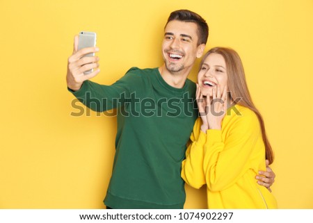Young lovely couple taking selfie against color background