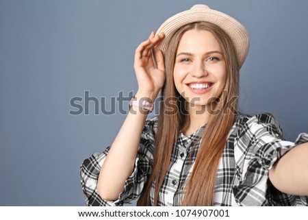 Young beautiful woman taking selfie against grey background