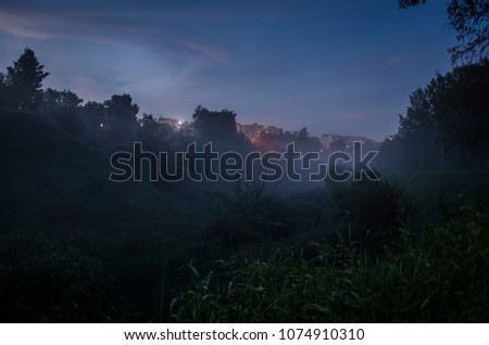 The ravine outside the city in the fog in the evening. Lights of multi-story houses Royalty-Free Stock Photo #1074910310