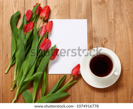 tulips are on wooden boards, cup of coffee, blank paper sheet for text, greeting concept