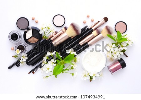 Makeup brush and decorative cosmetics with blooming branch on white background. Top view
