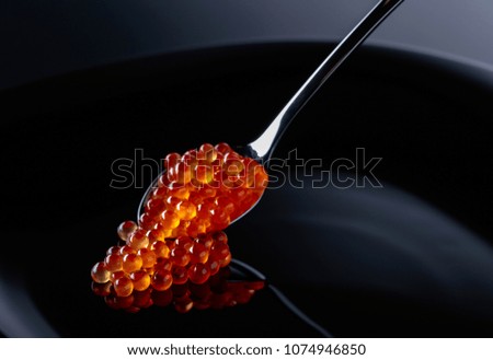  Red caviar in spoon on a black background.
