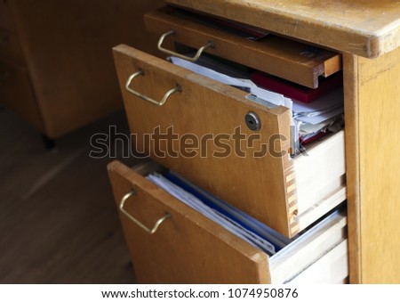 Closeup photo of old wooden desk with half-open drawers filled with papers.  Royalty-Free Stock Photo #1074950876