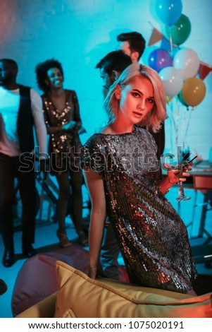 Glamorous woman holding glass with cocktail by friends at party