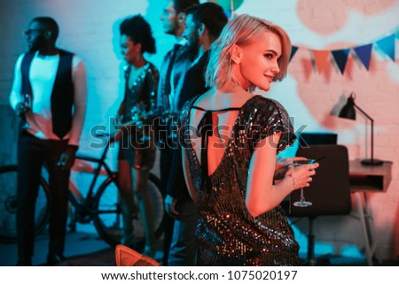 Blonde woman holding glass with cocktail by friends at party