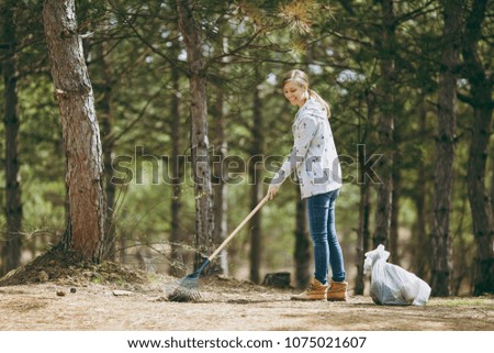 Young smiling beautiful woman cleaning and using rake for garbage collection near trash bags in park or forest. Problem of environmental pollution. Stop nature garbage, environment protection concept