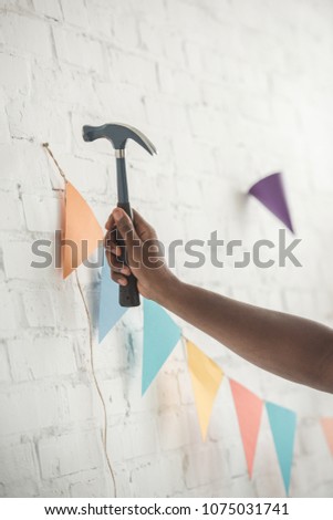 cropped image of man nailing up string with party garland on brick wall 