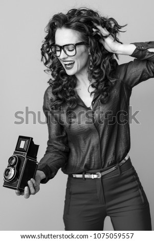 happy trendy woman with long wavy brunette hair using retro photo camera isolated on background