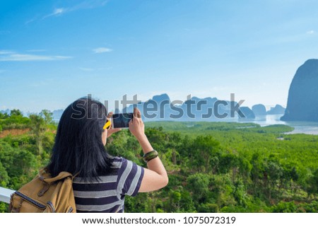 Young traveler woman backpacker use mobile phone take a photo of beautiful of sunrise nature at top of mountain view,Freedom wanderlust concept,Khao Samed Nang Chee,Phang Nga,Thailand.