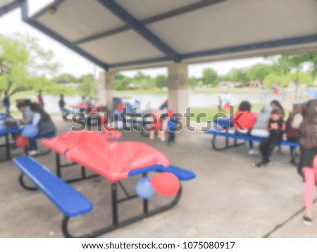 Blurred abstract birthday celebration at pavilion in Texas, USA. Group party with balloon decoration, metal picnic tables at public park shelter. Lake in background