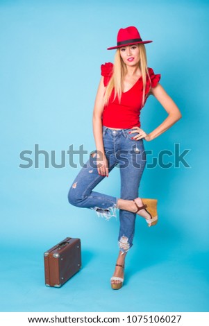 Summer, travel and vacation concept - Portrait of a beautiful young blonde woman with retro suitcase on blue background.
