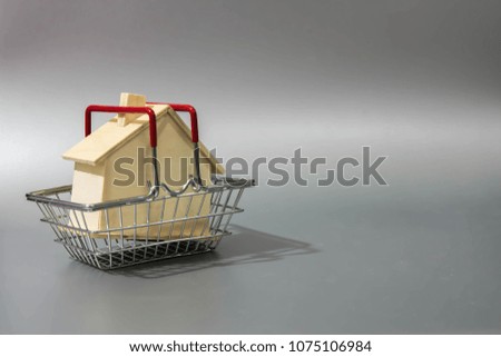 Miniature little wood house in mini shopping cart on gray background. Image for property real estate investment concept. Home for sale in market. (selective focus )