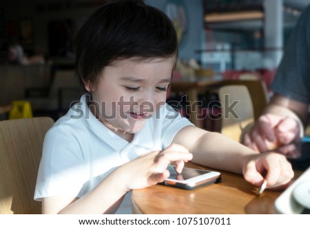School boy playing game on mobile phone at the coffee shop,Cute little boy sitting in the cafe watching cartoons on phone with parent, Happy child having fun and relaxing after school.