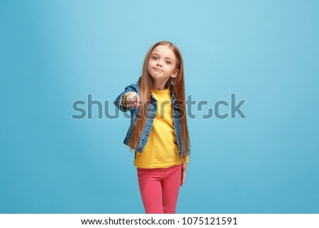 I choose you and order. The smiling teen girl pointing to camera, half length closeup portrait on blue studio background. The human emotions, facial expression concept. Front view. Trendy colors