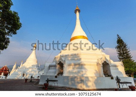 Golden sun light shining on white and gold pagoda with dark blue sky in in background