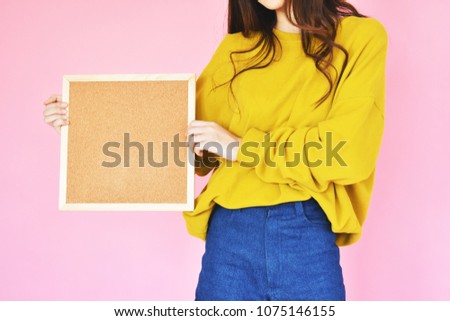 girl holding empty cork board in casual clothes standing on pink background