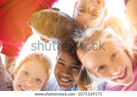 Portrait of happy kids in circle looking down and embracing. Group of five multiethnic friends outdoor looking at camera and smiling. Closeup face of children looking at camera together at park. Royalty-Free Stock Photo #1075169171