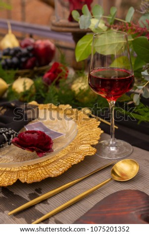 A red rosebud, lying on a golden platter, next to a glass of red wine, a golden spoon and a knife, golden fruits and flowers on an old wooden table. Decoration, gothic wedding. Copy space.