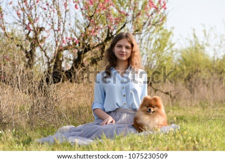 A young girl sits on the grass with a dog in a peach orchard