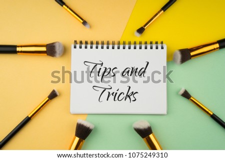 Cosmetics product arranged creatively on a colored background with "Tips and Tricks" text on a spiral notebook. Beauty concept. Top view or flatlay. 