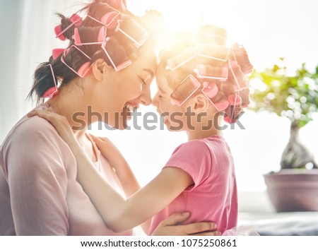 Happy loving family. Mother and daughter are doing hair and having fun. Mom and her child girl playing, kissing and hugging.