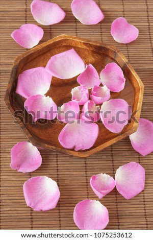 pink roses petals in bowl with water on bamboo background, spa concept