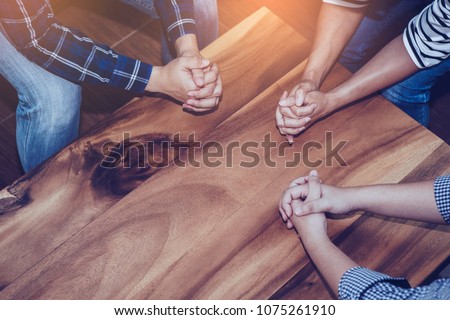 Christian people prays together around wooden table. prayer meeting small group concept. Royalty-Free Stock Photo #1075261910