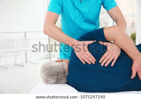 Young physiotherapist working with senior patient in clinic Royalty-Free Stock Photo #1075297190
