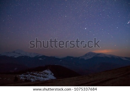 Majestic view of fantastic starry dark sky over magnificent Carpathian mountains covered with evergreen forest and snow-capped peaks in distance. Breathtaking panorama of beauty and magic of nature.