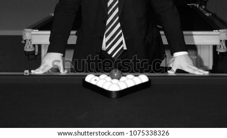 a man in a suit leans his hands on a pool table, on which billiard balls are in a triangular frame. Black and white picture