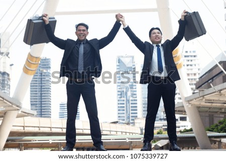 Businessman with partner keeping arms raised and expressing happy  celebrating his success while standing outdoor office.