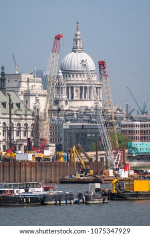 London skyline showing the iconic dome of St Paul's Cathedral and other buildings, as well as cranes and buildings under construction. Photo taken on a clear spring day, with pastel blue sky.