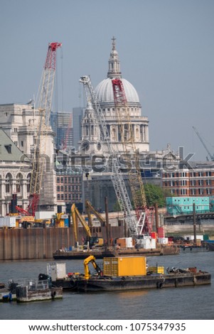 London skyline showing the iconic dome of St Paul's Cathedral and other buildings, as well as cranes and buildings under construction. Photo taken on a clear spring day, with pastel blue sky.