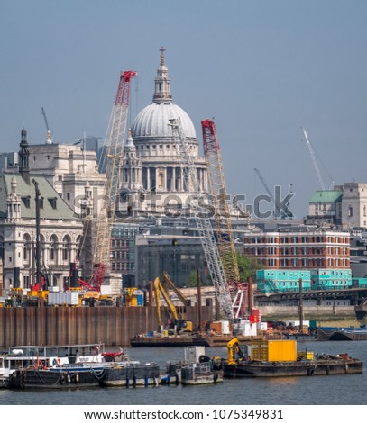 London skyline showing the dome of St Paul's Cathedral and other buildings in the vicinity, as well as cranes and buildings under construction. Photo taken on a clear spring day, with pastel blue sky.
