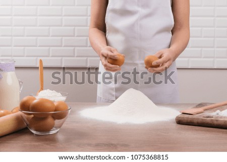 The chef in white apron sifts the flour through a sieve to prepare the dough for pizza on a light background. Happy young mother making dough. 