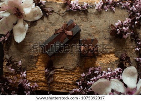 Top view. Box. Black box with brown bow. Gold rings. Green leafs. Blur table. Spring fruit trees white flowers photo. Natural wooden background with white flowers fruit trees and space for text