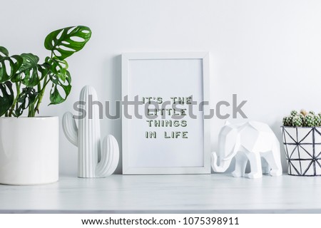 Creative desk with mock up white frame, cacti, elephant figure and plant. White wall background. Modern interior.