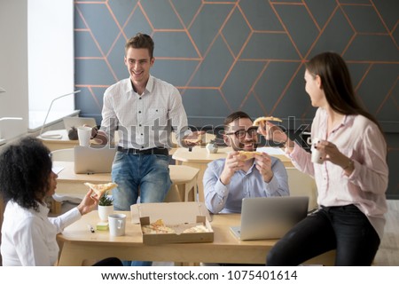 Friendly diverse team talking and laughing eating pizza together, happy colleagues sharing meal, multiracial coworkers group enjoying lunch at break, good relations and office food delivery concept