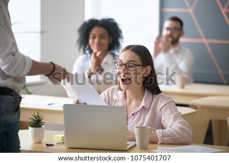 Excited successful student receiving document from boss with good result, colleagues congratulating happy millennial promoted rewarded employee amazed by great news in written notice with applause Royalty-Free Stock Photo #1075401707