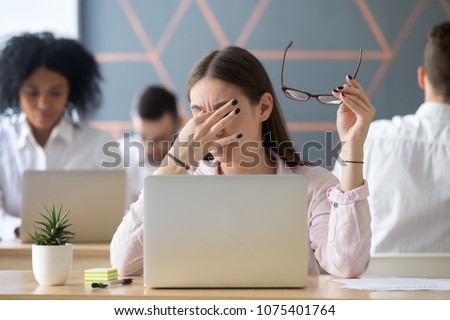 Young woman taking off glasses tired of computer work, exhausted student or employee suffering from eye strain tension or computer blurry vision problem after long laptop use, eyes fatigue concept Royalty-Free Stock Photo #1075401764