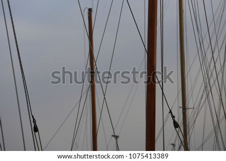 Pattern of wooden matts and many ropes in a french marina. Graphic image with oblique and vertical lines. Silhouette of parts of sailboats with a grey sky in background Abstract image of navigation. 
