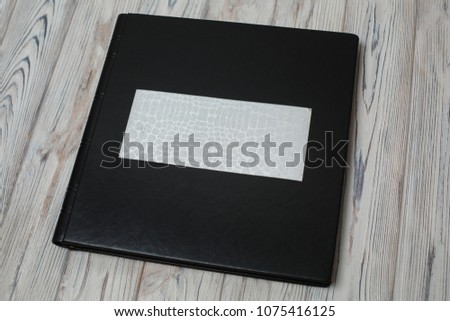 black leather photo book on wooden background.
photobook with a shield on a  light background. dark family photo album.wedding photoalbum.