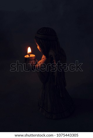 angel holds a burning candle in the dark. background religion, prayer and faith.