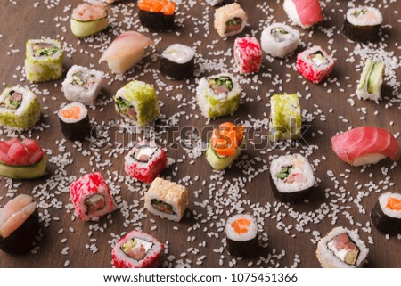 Japanese traditional cuisine. Delicious set of various sushi, rolls and gunkans served on rustic wooden background with spilled rice.