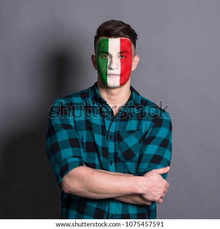 Face of young man painted with flag of Italy. Football or soccer team fan, sport event, faceart and patriotism concept. Studio shot at gray background, copy space