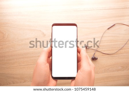 Technology concept, Woman hand holding smartphone on wood table with black headphone cable background,top view.