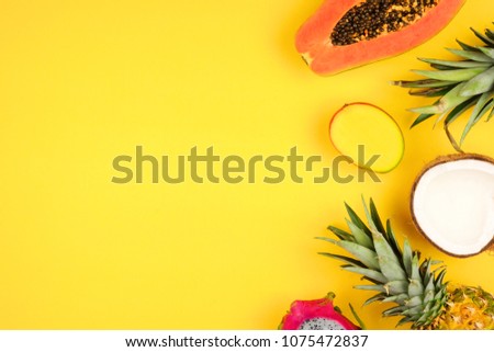 Tropical fruit side border with pineapple, dragon fruit, papaya, coconut and mango on a bright yellow background